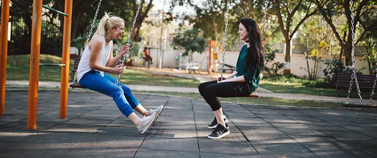 Two women sitting on swings, facing each other.